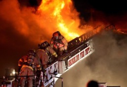 Three firefighters climbing engine ladder into fire