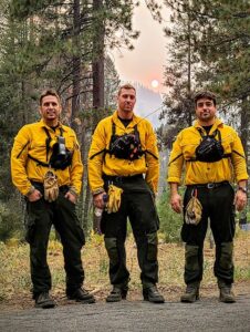Three Firefighters posing in front of wild fire in distance